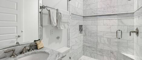 A modern bathroom with a marble sink, a toilet, and a shower area.