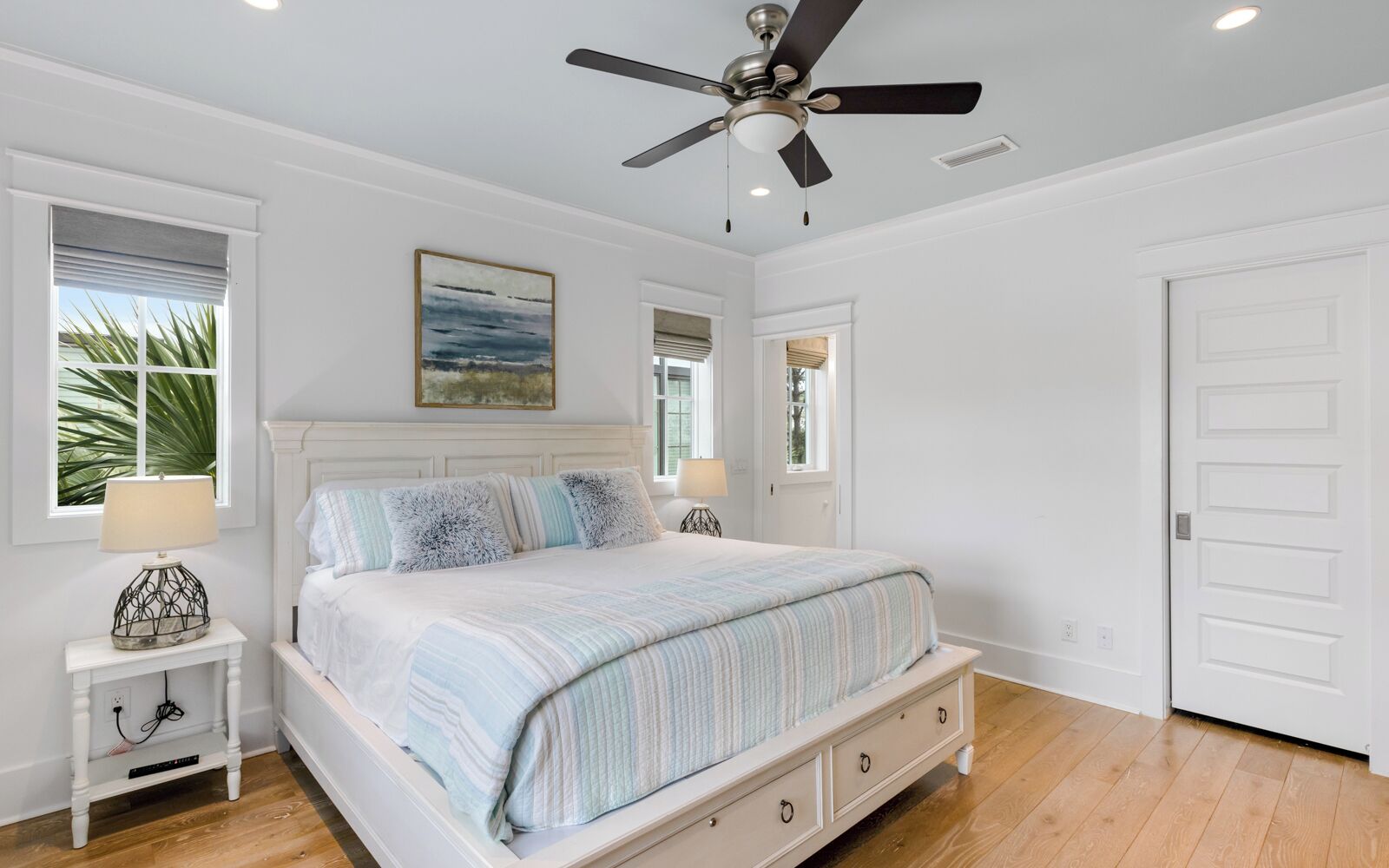 A bedroom with a bed, nightstands, a ceiling fan, and a door.