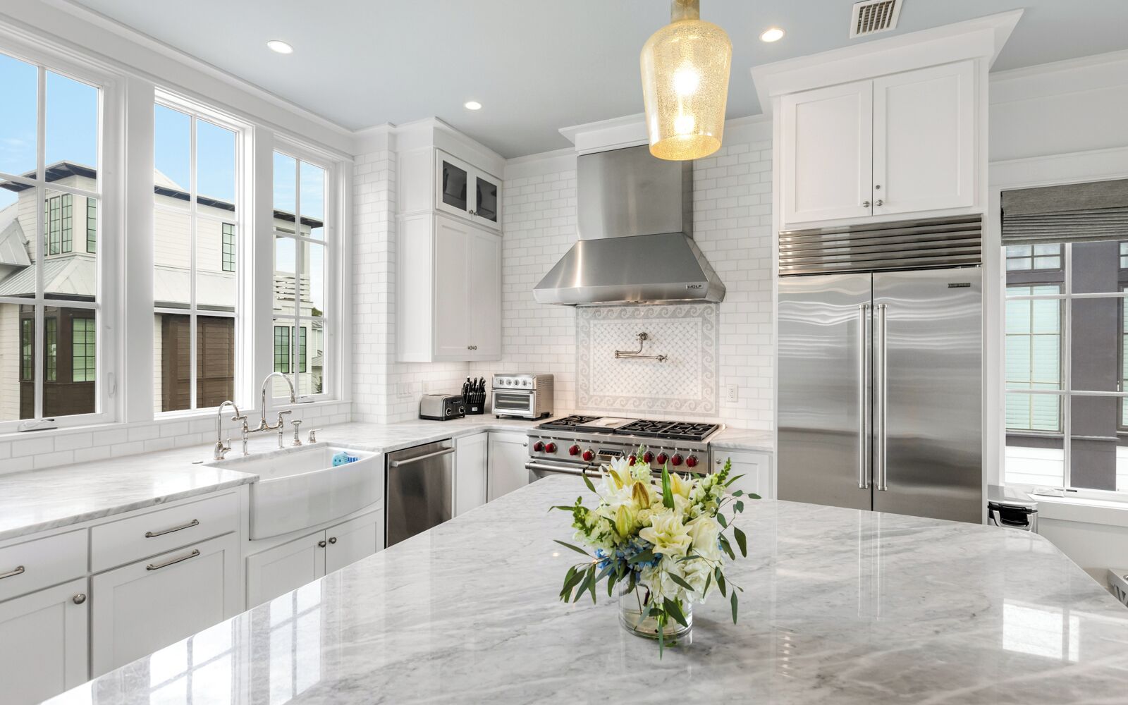 A modern kitchen with white cabinetry, a central island, a stainless steel range, and a large window providing natural light.