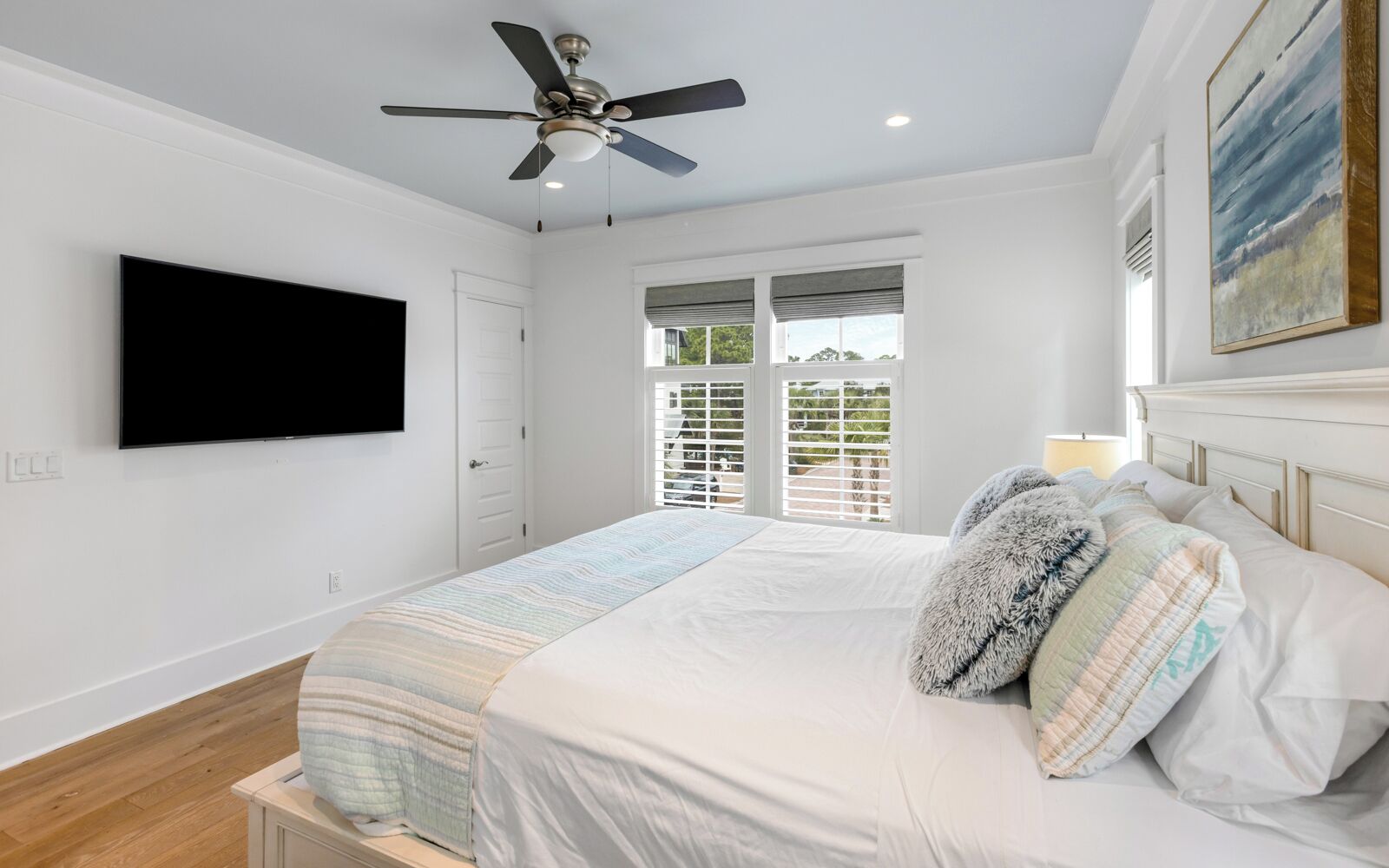 A bedroom with a bed, a ceiling fan, a TV, and a window with blinds.