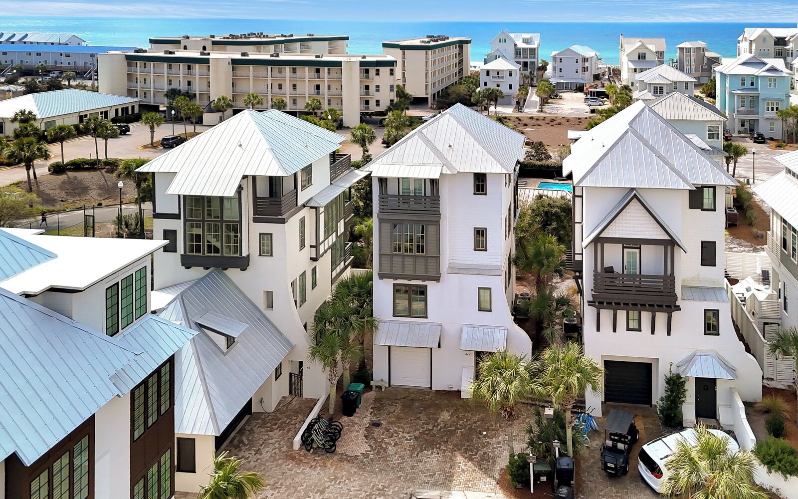Ein Küstenwohngebiet mit modernen Häusern, die Giebel und Balkone haben, einem gepflasterten Innenhof und Blick aufs Meer.