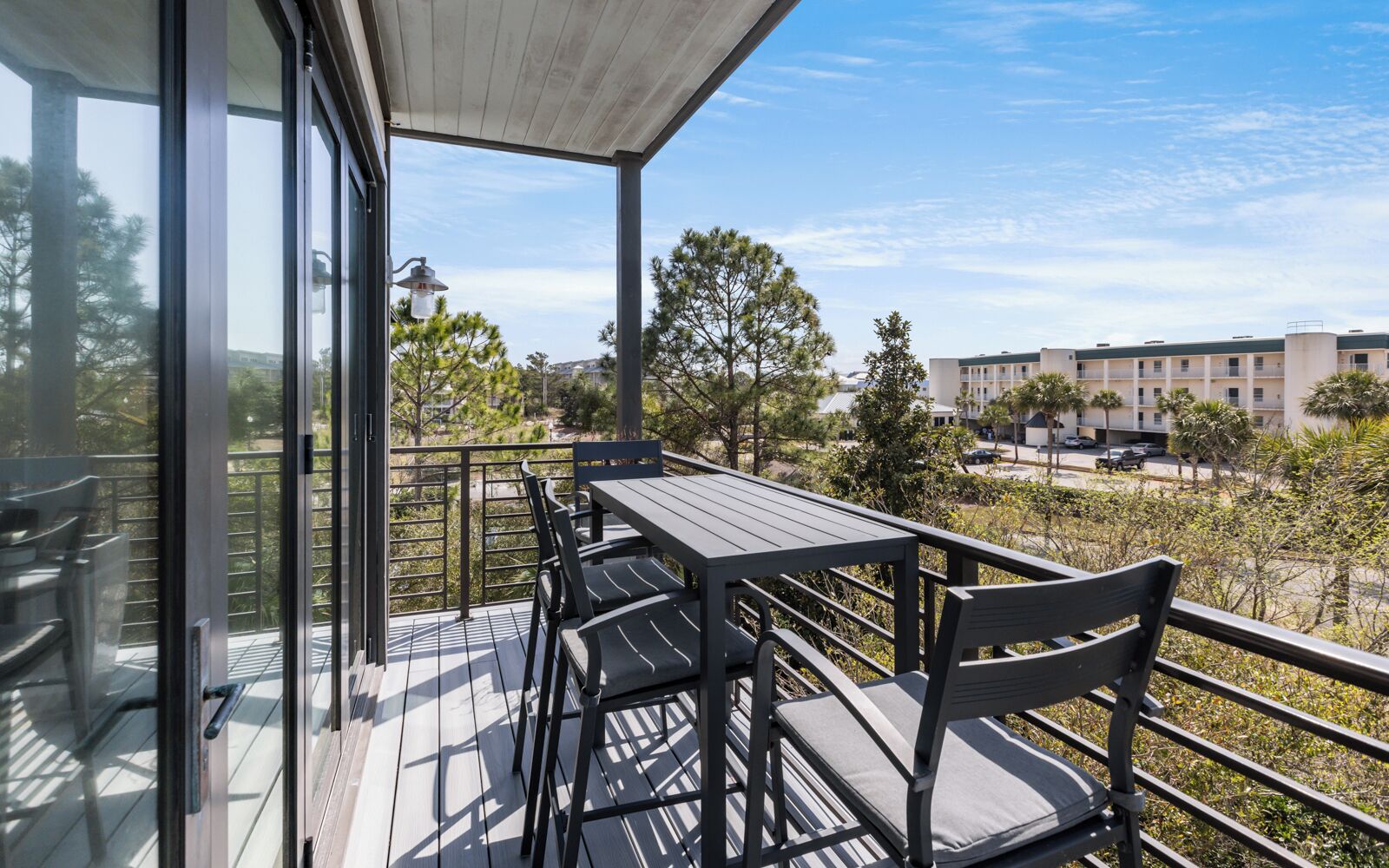 Un balcon avec une table et des chaises, donnant sur un quartier résidentiel bordé d’arbres et de bâtiments.
