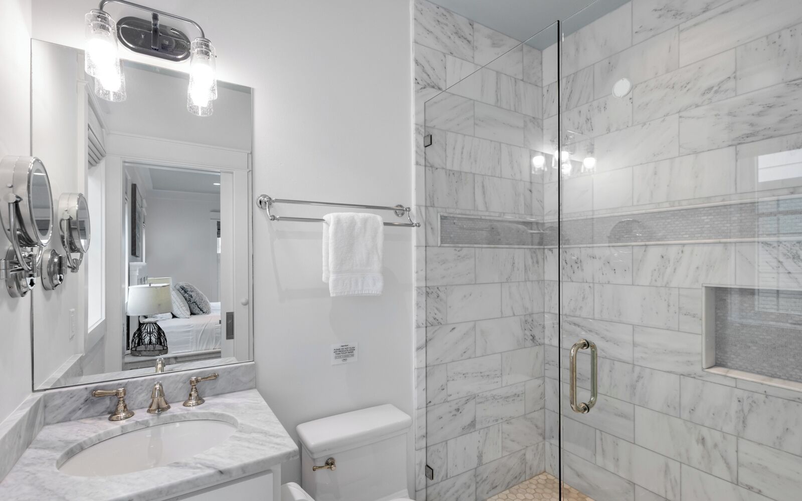 A modern bathroom with a marble sink, a large mirror, a glass-enclosed shower, and a towel rack.