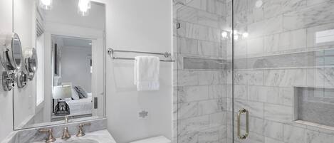 A modern bathroom with a marble sink, a large mirror, a glass-enclosed shower, and a towel rack.