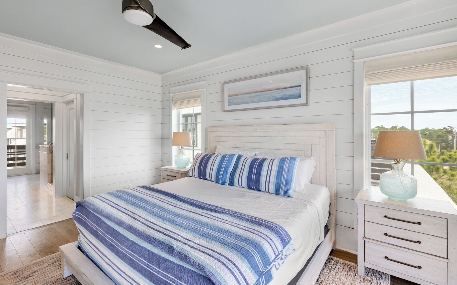 A bedroom with a large bed, a nightstand, a lamp, and a window with a view.