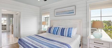 A bedroom with a large bed, a nightstand, a lamp, and a window with a view.