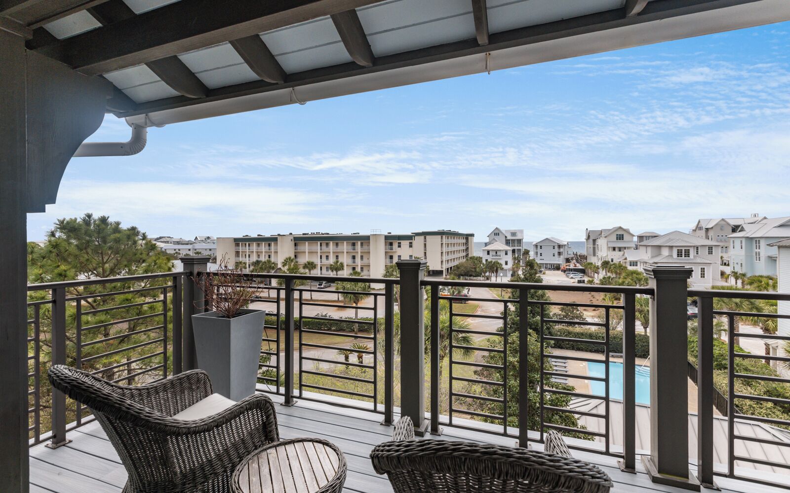 A balcony with wicker furniture, a view of a swimming pool, and residential buildings in the background.