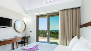 A hotel room with a bed, a desk with a chair, a TV, and a large window with a view of the sea. - Villa Estel | Estel Residences (Chania)