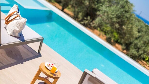 A poolside area with lounge chairs and a small table with a drink. - Villa Estel | Estel Residences (Chania)