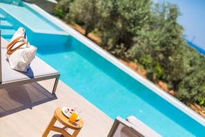 A poolside area with lounge chairs and a small table with a drink. - Villa Estel | Estel Residences (Chania)