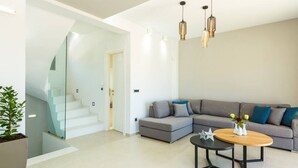 A modern living room with a grey sectional sofa, a wooden coffee table, and a staircase leading to another level. - Villa Estel | Estel Residences (Chania)
