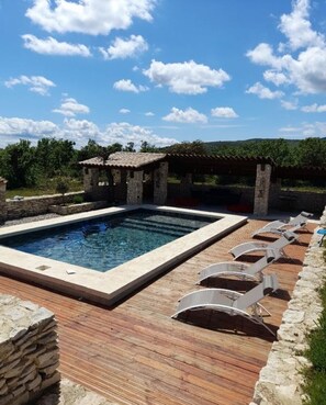 Relax by the pool surrounded by a wooden deck and a stone structure.