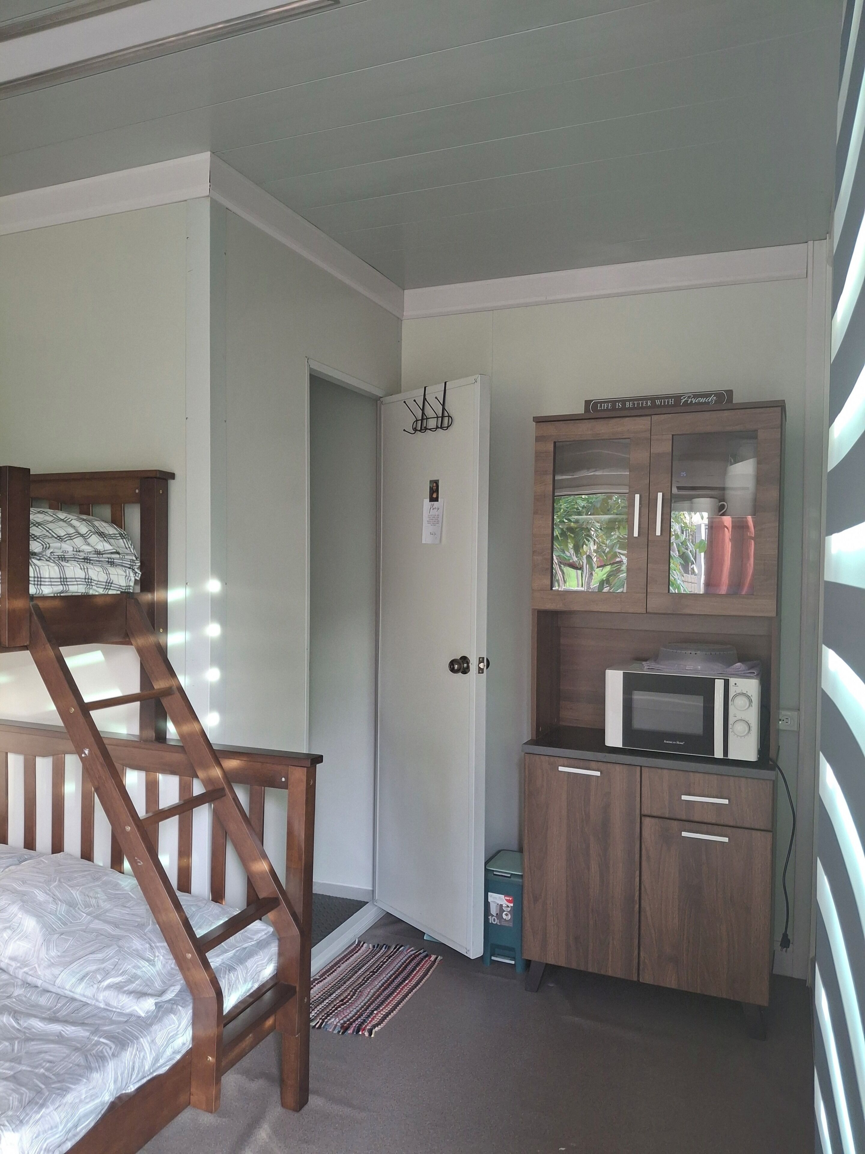 Une chambre avec un lit en bois, une porte blanche, une petite kitchenette équipée d’un four à micro-ondes et un placard.