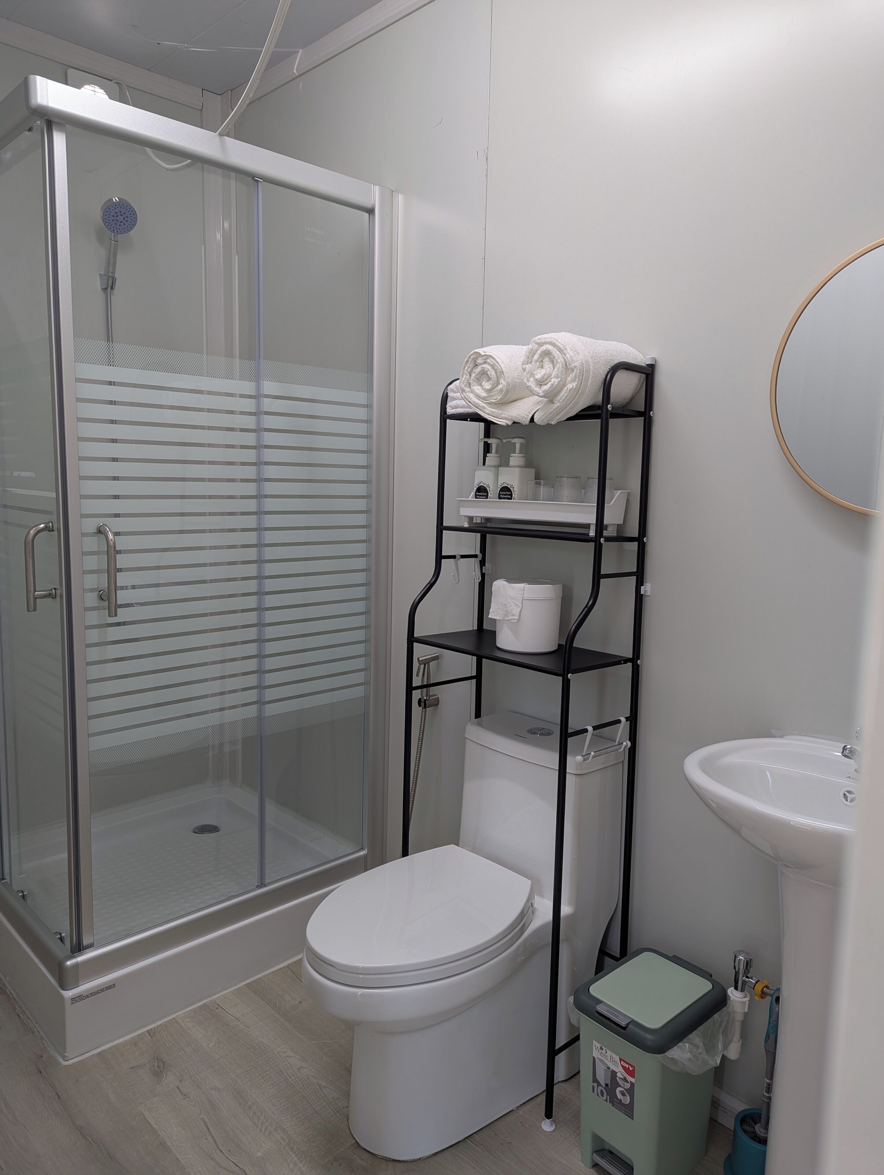 A modern bathroom with a glass-enclosed shower, a toilet, a sink, and a shelf with toiletries.