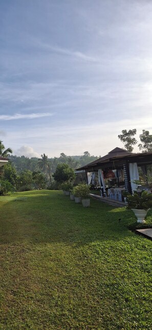 A grassy area with a building that has a covered patio with chairs and tables. - Asuneus Farm (Carmen)