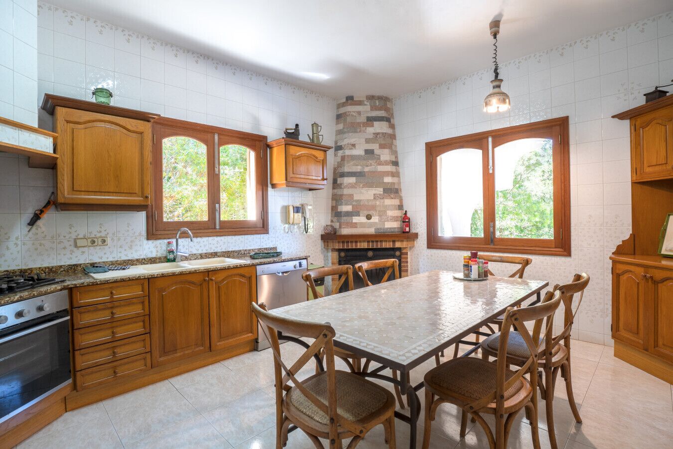 A kitchen with wooden cabinets, a stone fireplace, and a dining table with chairs.