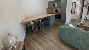 A modern kitchen with a wooden countertop, bar stools, and a microwave. There is a green sofa and a globe on a wooden table. - Résidence de la Place (Pont-du-Château)