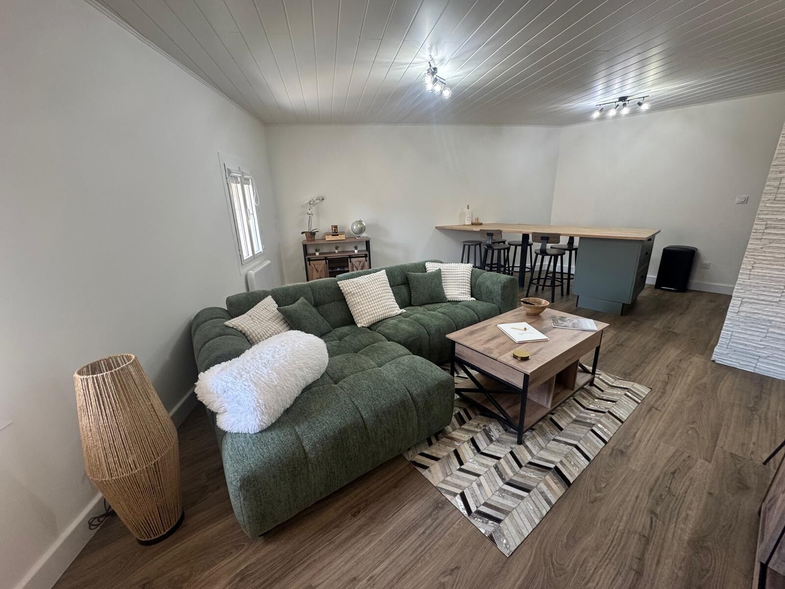 A modern living room with a green sectional sofa, a wooden coffee table, and a herringbone-patterned rug.