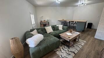 A modern living room with a green sectional sofa, a wooden coffee table, and a herringbone-patterned rug.