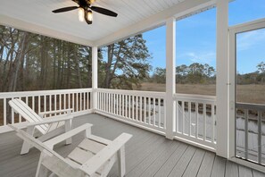 A covered outdoor deck with white railings, two lounge chairs, and a ceiling fan.