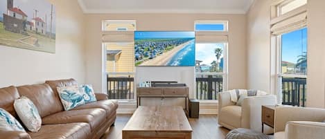 Un salón amplio con un televisor de pantalla plana grande, sofás de cuero, una mesa de centro de madera y un balcón con vistas a la playa.