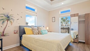 A bedroom with a large bed, a nightstand, and a wardrobe. There are two windows with views of palm trees and a balcony. - Nauti By Nature 3 Bedroom Home (Port Bolivar)