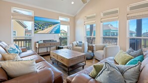 A spacious living room with a large TV, leather sofas, a wooden coffee table, and a ceiling fan. - Nauti By Nature 3 Bedroom Home (Port Bolivar)