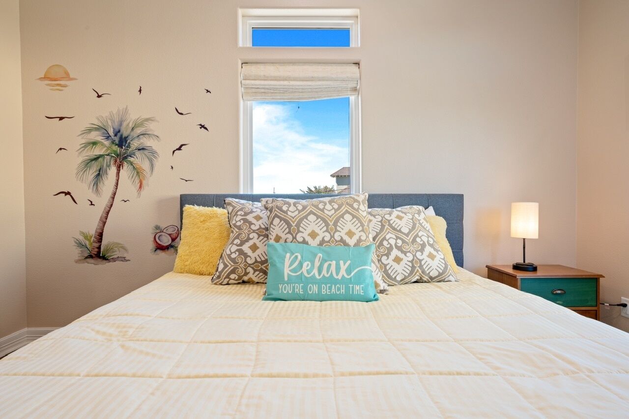 A bedroom with a bed, pillows, a nightstand, a lamp, and a window with a view.