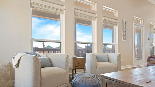 A spacious living room with large windows, a wooden coffee table, and a comfortable sofa. - Nauti By Nature 3 Bedroom Home (Port Bolivar)
