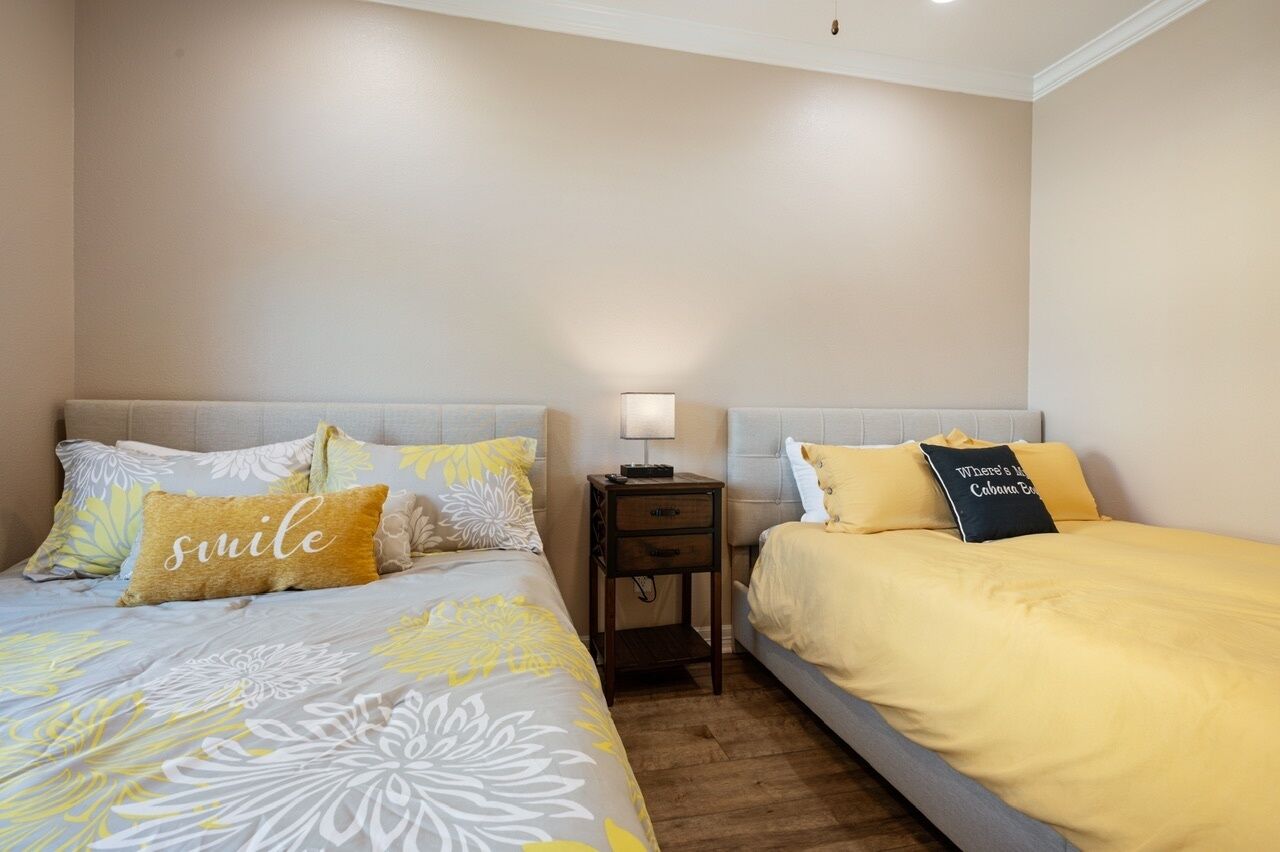 Une chambre d’hôtel avec deux lits, chacun recouvert d’une couvre-lit d’une couleur différente, une table de chevet avec une lampe et un luminaire fixé au mur.