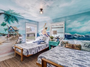 Enjoy a coastal ambiance in this room, featuring a beach-themed mural and two beds with matching headboards.