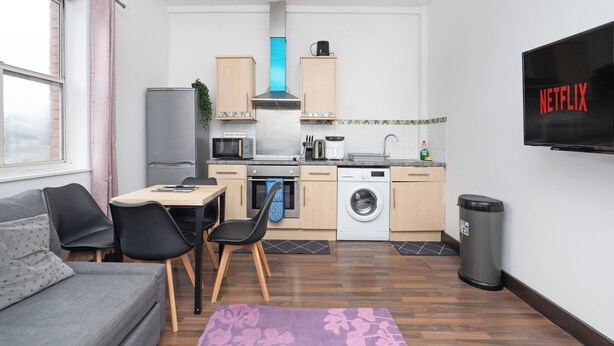 Ein kompakter Wohnbereich mit Küchenzeile, Essplatz, einer Couch und einem an der Wand befestigten Fernseher.