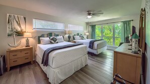 A bedroom with two beds, a desk, a chair, a ceiling fan, and a large window with curtains.