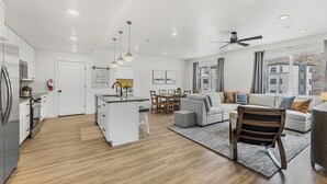 A modern kitchen with white cabinets, a dining area with a table and chairs, a gray sofa, and a ceiling fan. - Starlight Crossing 4 Bedroom Condo (Hurricane)