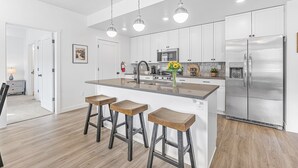 A modern kitchen with white cabinets, stainless steel appliances, and a central island with bar stools. - Starlight Crossing 4 Bedroom Condo (Hurricane)