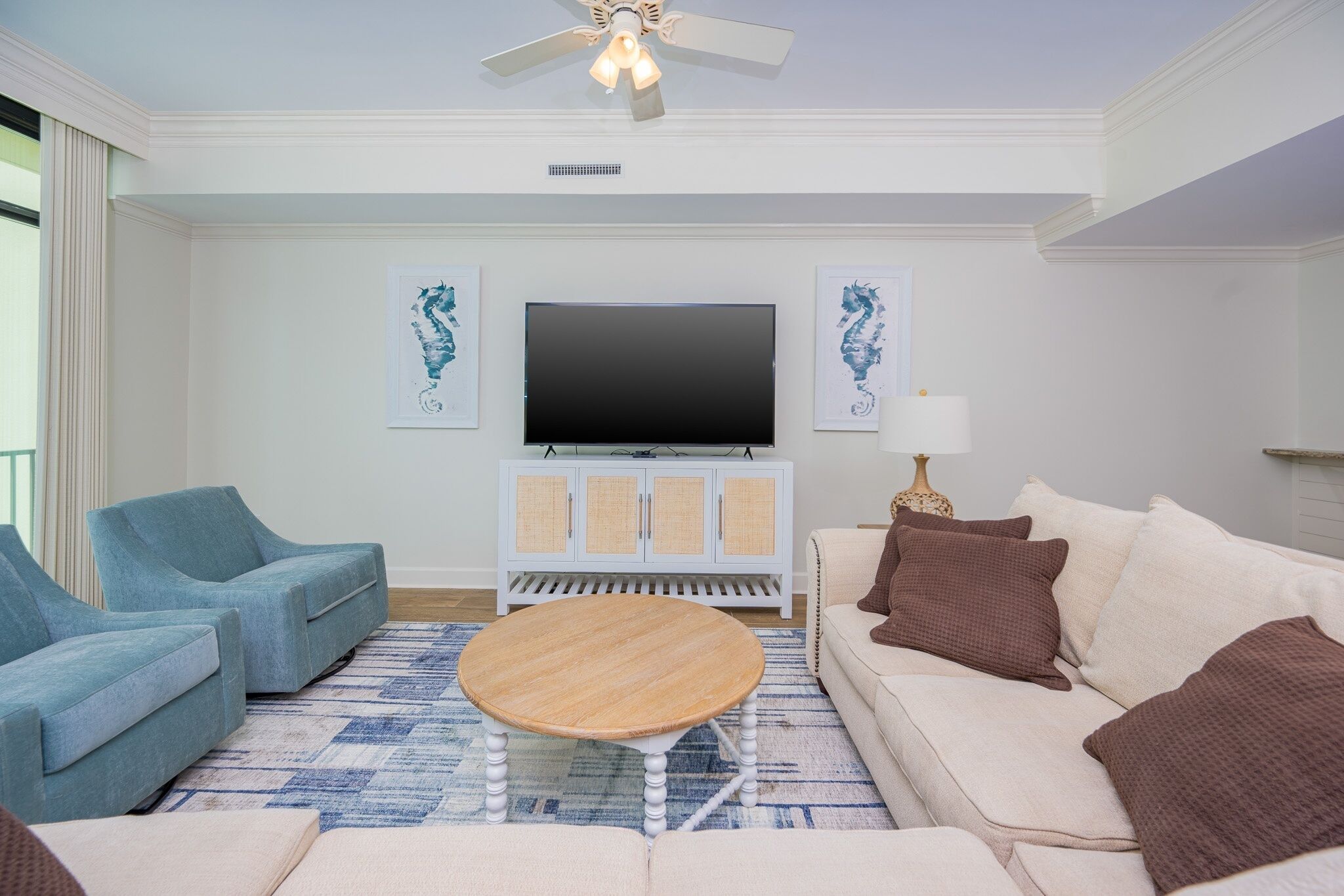 A living room with a flat-screen TV, two sofas, a coffee table, and a ceiling fan.