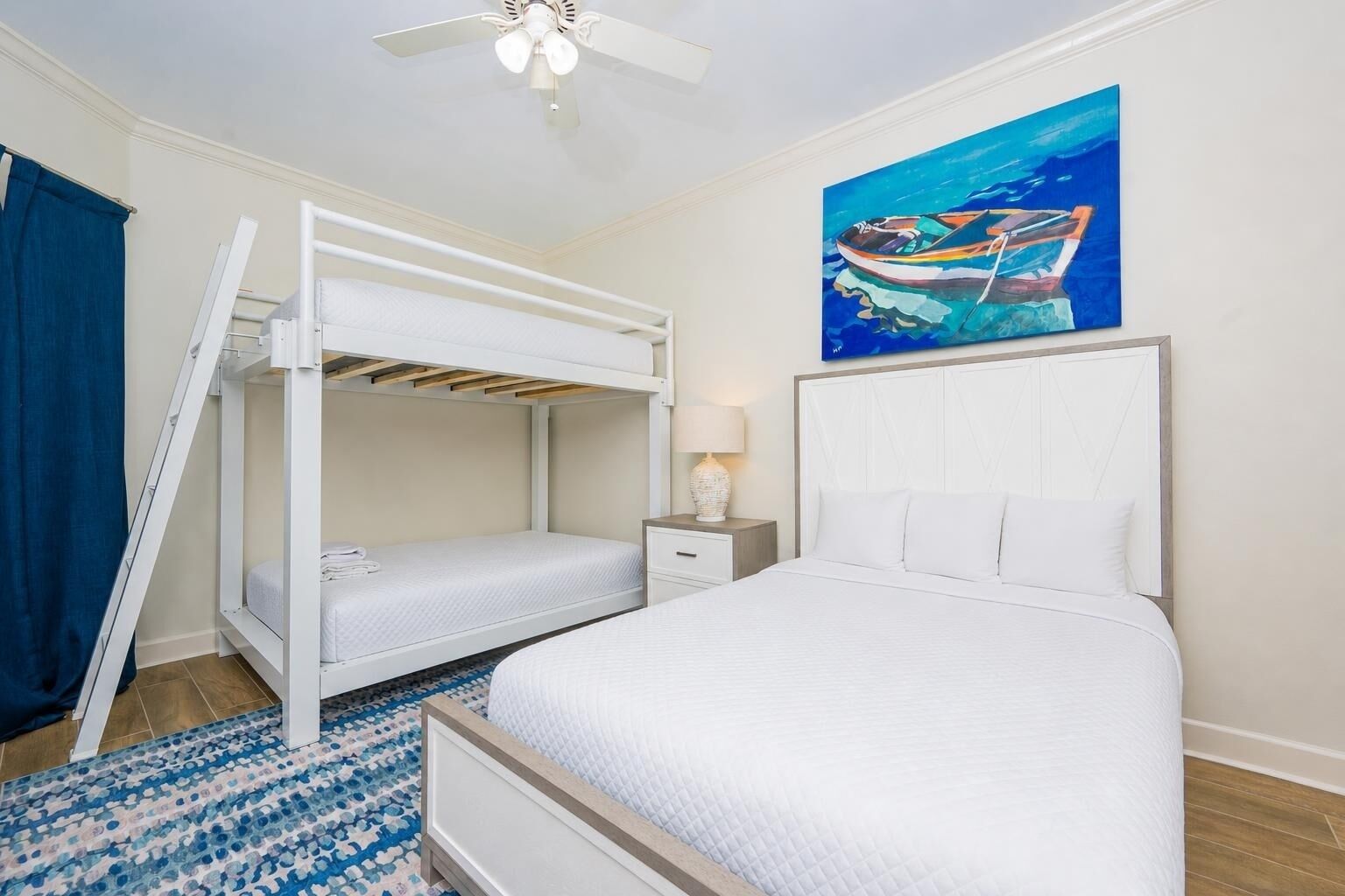 Un dormitorio con literas, una cama individual, una mesita de noche, una lámpara y un cuadro de un barco en la pared.