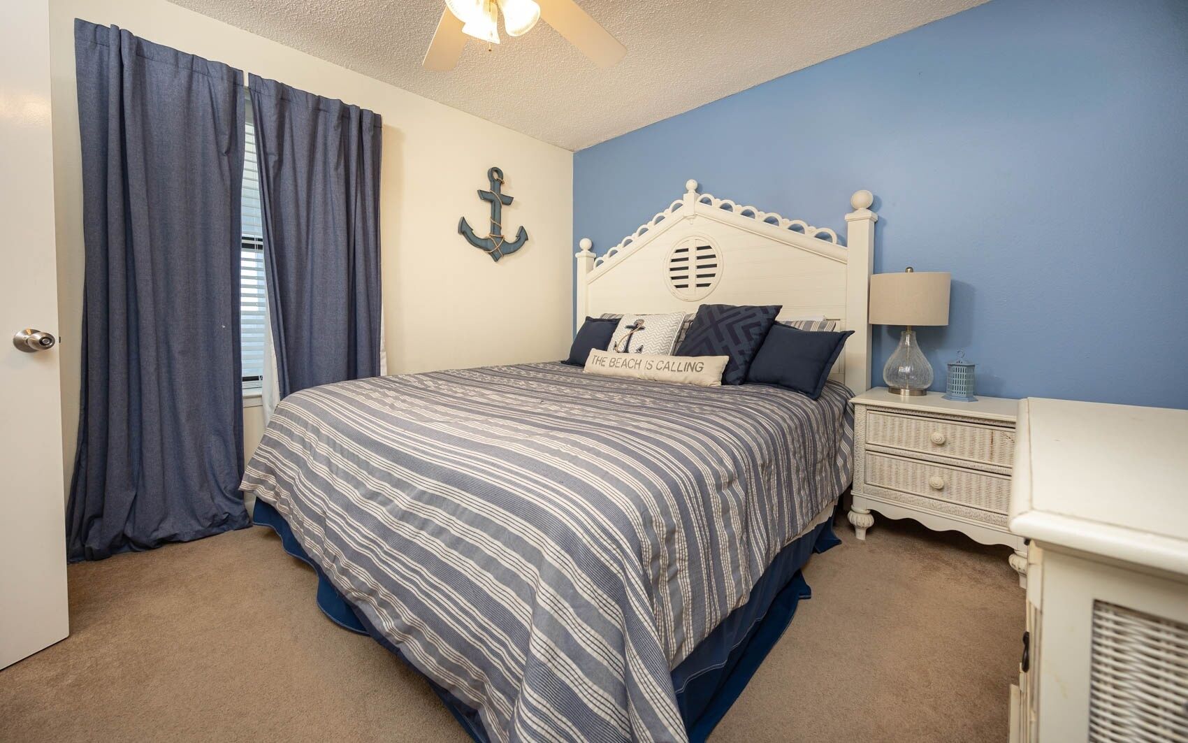 A bedroom with a bed, a nightstand, a lamp, and a wall anchor decoration.
