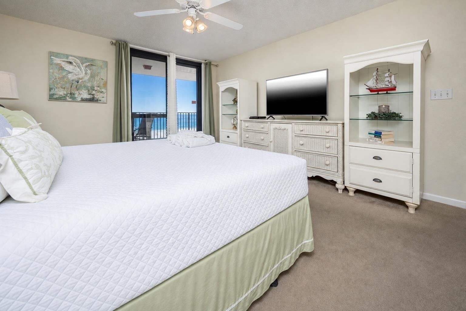 A hotel room with a large bed, a flat-screen TV, a dresser, and a view of the ocean.