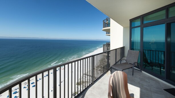 A balcony with a view of the ocean, a chair, and a glass door.
