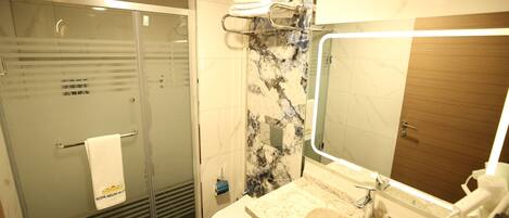 Un baño moderno con ducha de vidrio, inodoro, lavamanos con espejo y toallero con toallas.