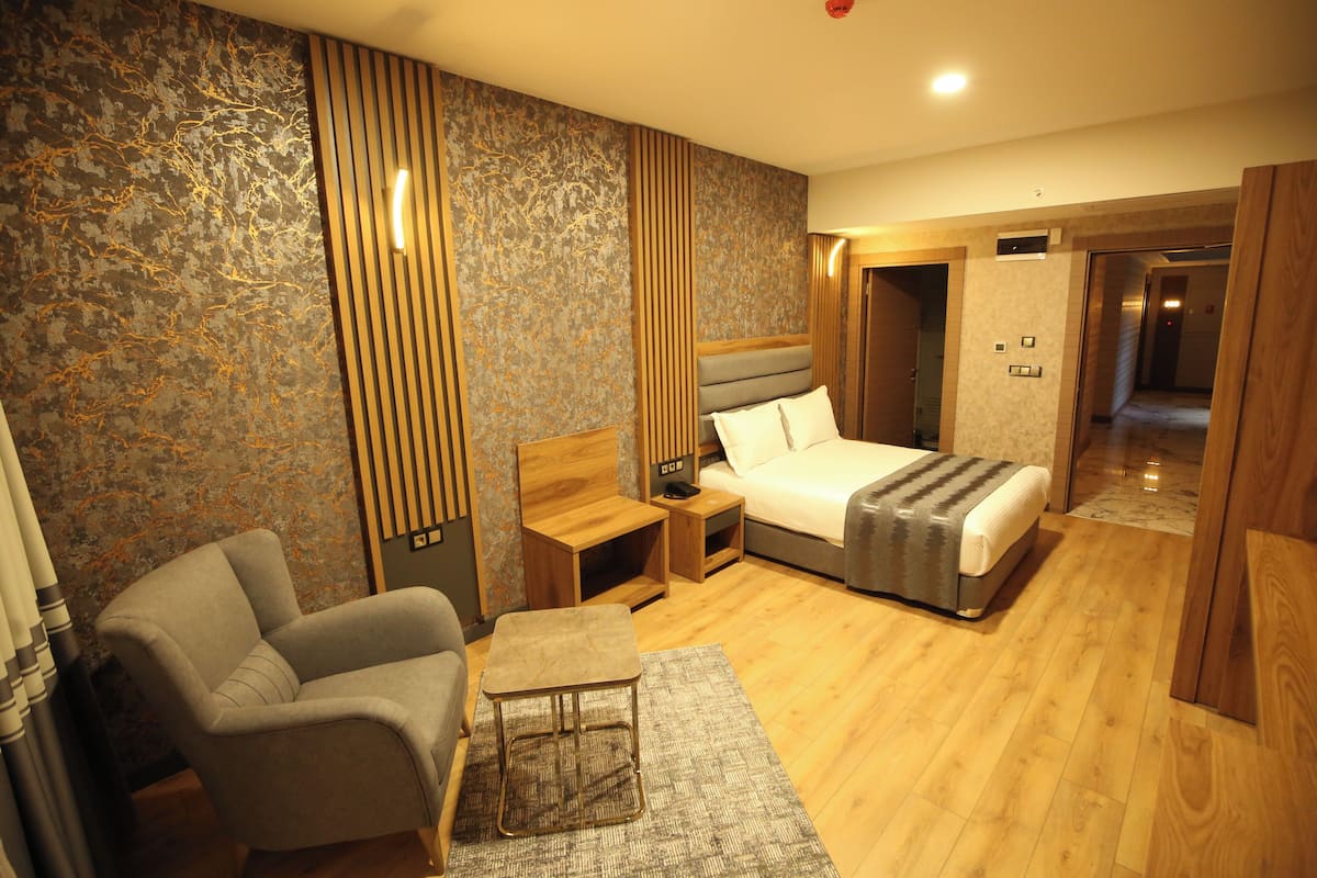 Quarto de hotel moderno com cama, poltrona, mesa pequena e mesa de cabeceira.