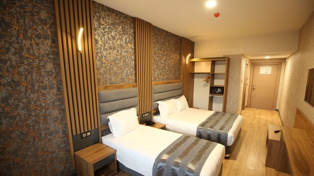 A hotel room with two beds, a wooden bench, a small table, a wardrobe, and a television. - Büpa delüxe hotel (Kayseri)