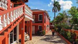 A red building with a tiled walkway and a person walking away. - Paradise On The Rocks Hotel (Negril)