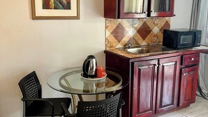 A compact kitchen with a round glass table, two black chairs, a microwave, and wooden cabinets. - Paradise On The Rocks Hotel (Negril)