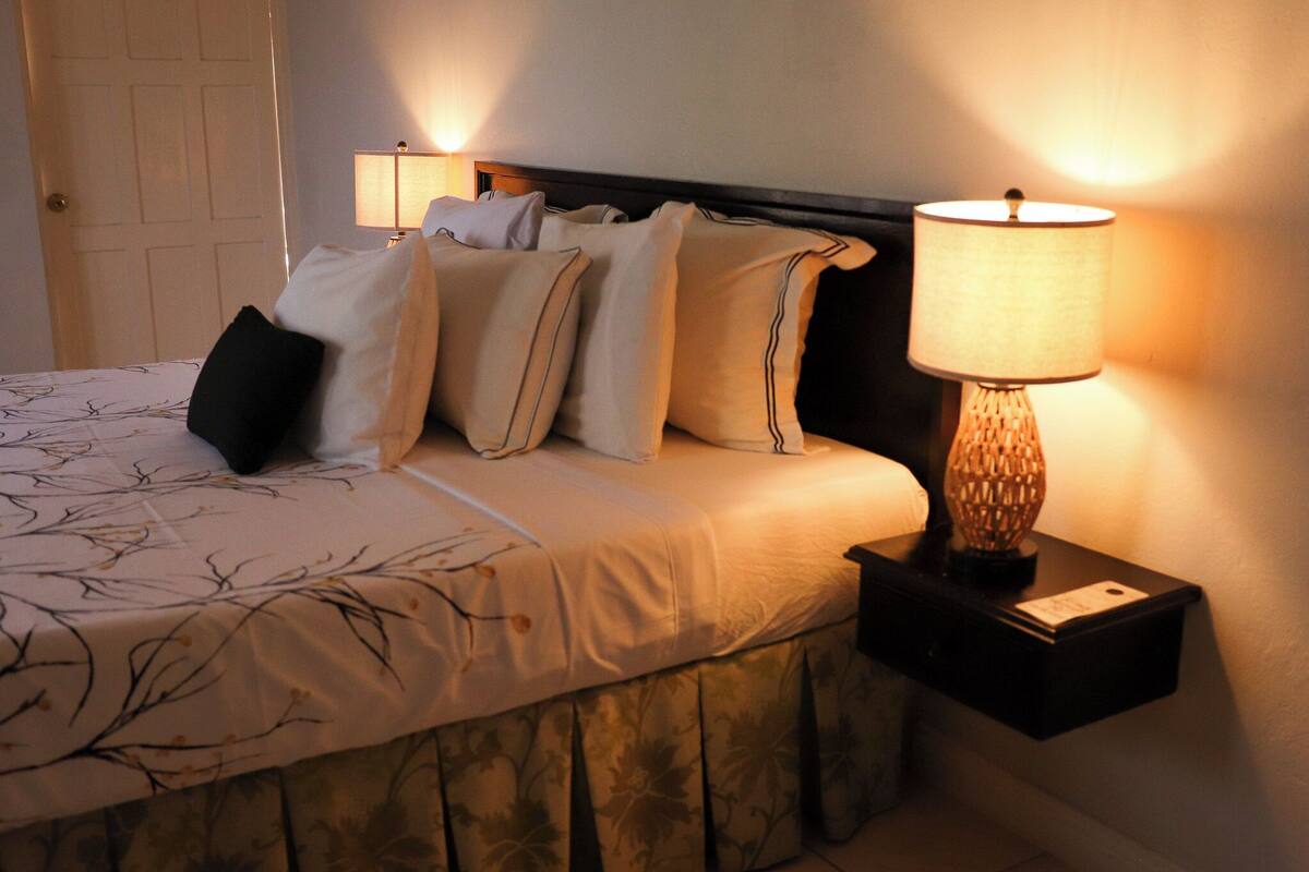A neatly made bed with multiple pillows, a bedside lamp, and a nightstand.
