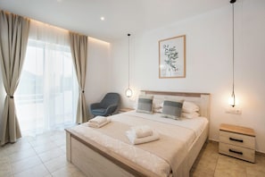 A hotel room with a bed, bedside tables, a chair, a wall-mounted picture, and a large window with curtains.