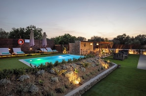 A pool with lounge chairs, a covered seating area, and a stone wall.