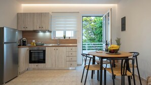 A modern kitchen with a built-in oven, a refrigerator, and a dining area with a table and chairs. - Kathys Apartment 1 in Archaggelos (Archangelos)