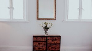 Une pièce comprenant une commode en bois, un miroir et un vase avec des plantes.
